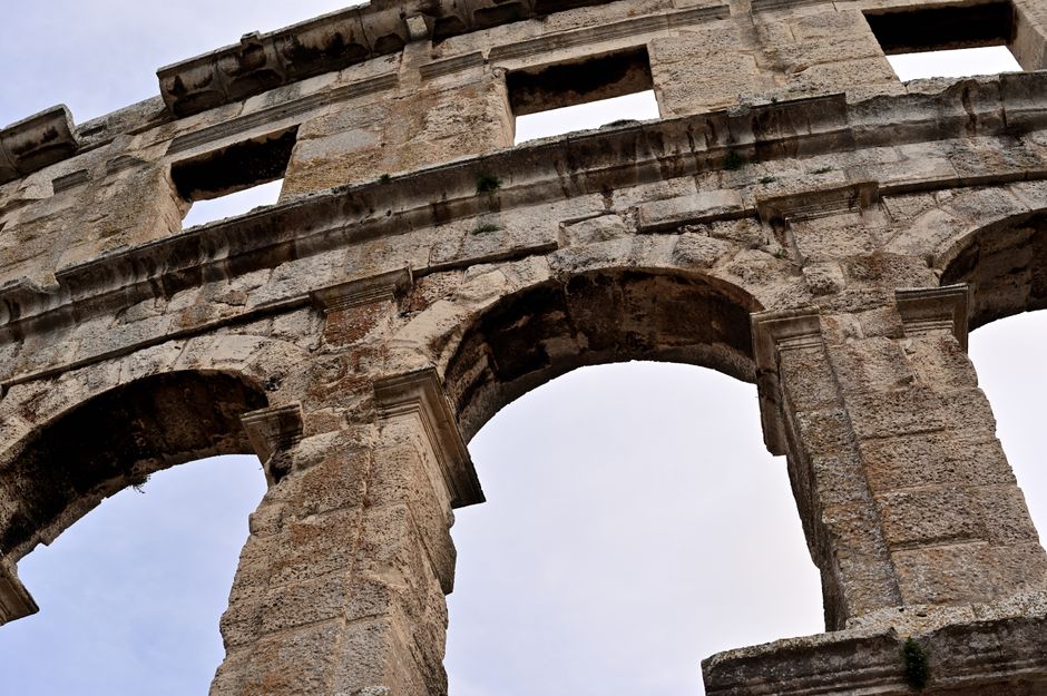 Low angle view of ancient Roman amphitheater ruins in Pula, Croatia, showcasing arches and stone structure.