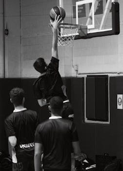 Dynamic black and white shot capturing a basketball player making a slam dunk indoors.