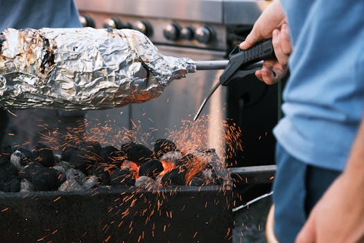 Barbecue cooking with foil-wrapped food over charcoal flames showing flying sparks and intense heat.