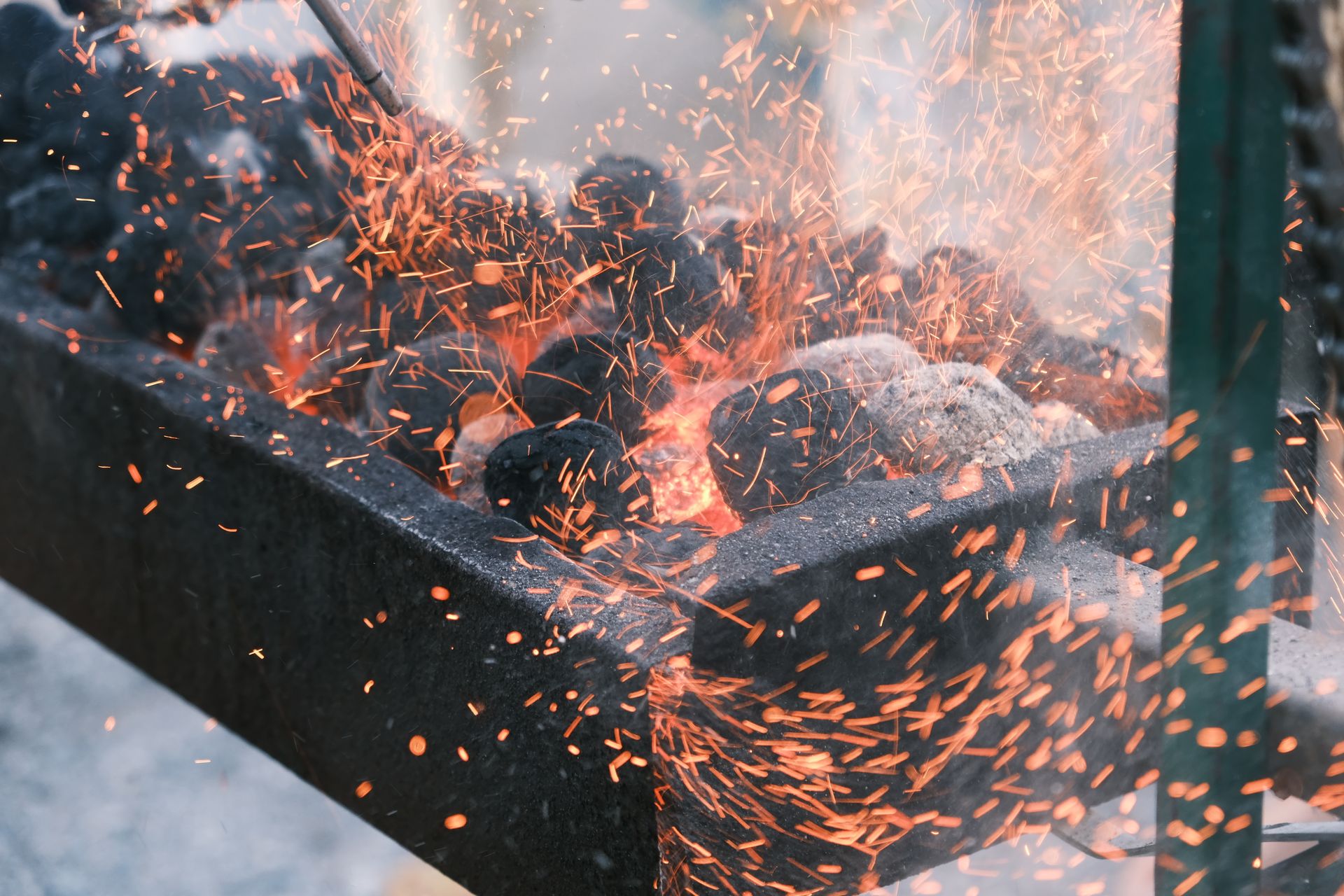 Close-up view of hot charcoal igniting with bright sparks flying upwards, showcasing intense heat energy.
