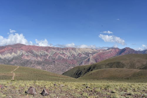 A Green Grass Field Near the Mountains Under the Blue Sky and White Clouds