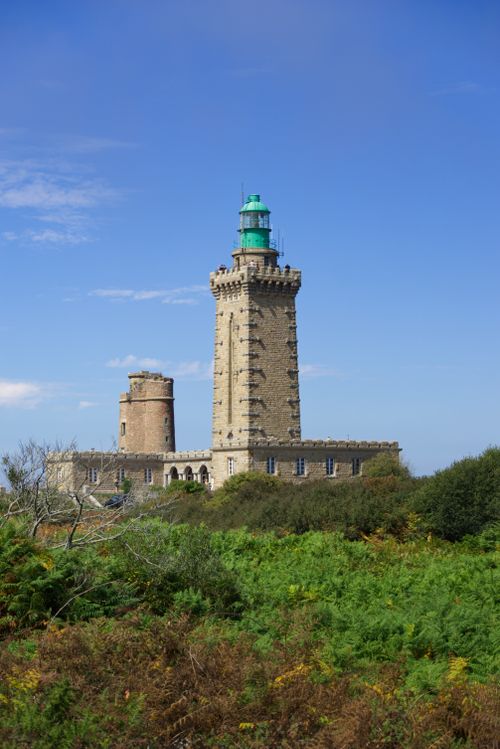 Free Explore the historic Cap Fréhel Lighthouse surrounded by lush greenery under a clear blue sky. Stock Photo