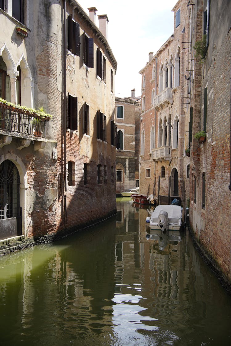 Boats On Body Of Water In Between Brick Buildings