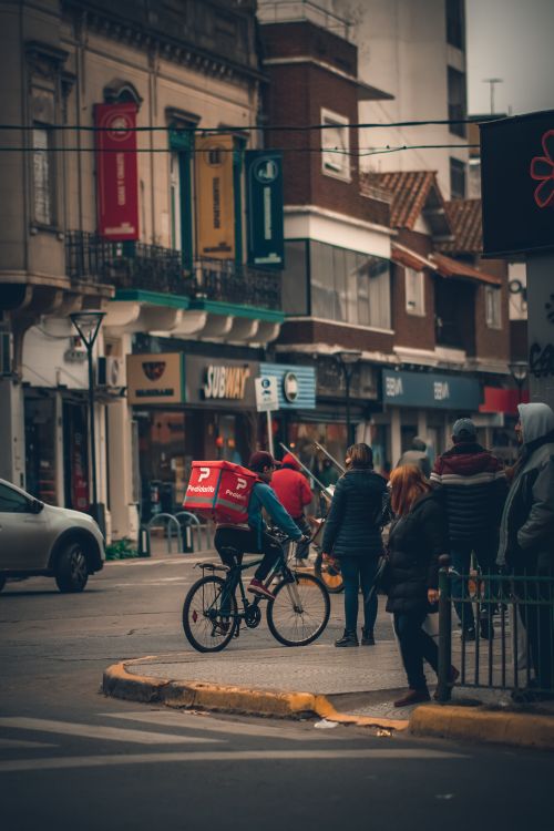 Free Urban street scene in Adrogué with a bicycle courier and pedestrians on a busy day. Stock Photo