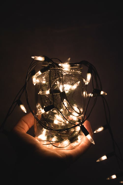 A Close-Up Shot of a Person Holding a Glass Jar with Christmas Lights