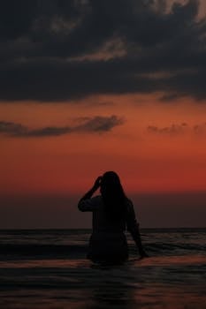Silhouette of a woman in the ocean at sunset, enjoying a peaceful moment.