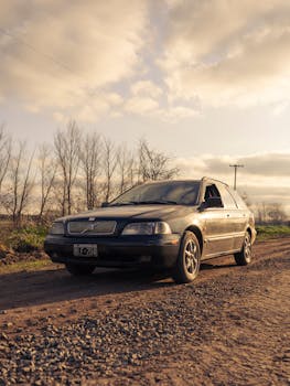 Compact sedan parked on a rural dirt road under a warm sunset sky.