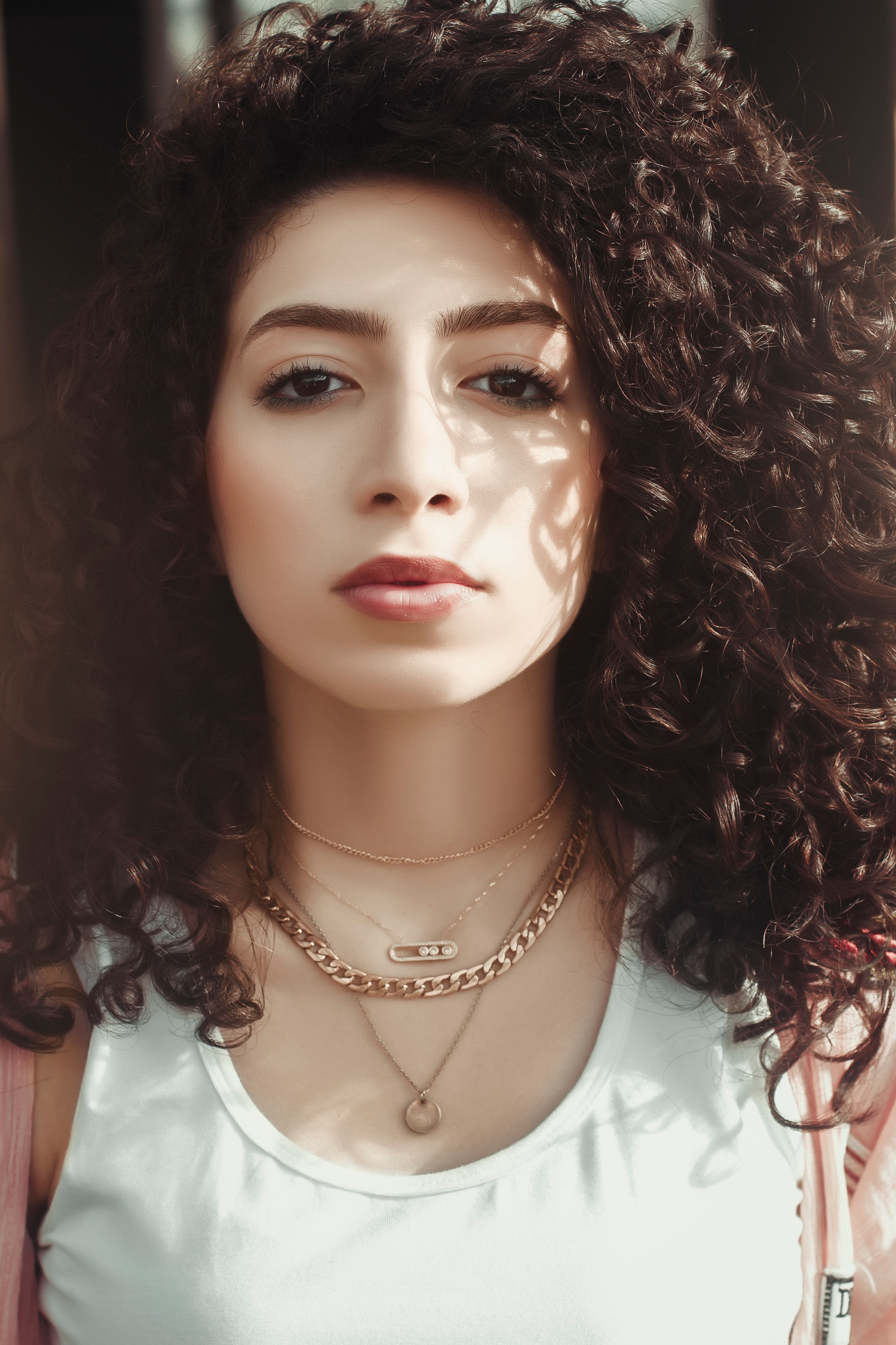 A vibrant close-up portrait highlighting a young woman with curly hair and layered necklaces.