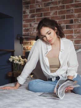 A young woman enjoys reading a magazine while relaxing in a stylish, modern bedroom setting.