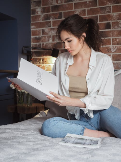 Woman Sitting on a Bed and Looking Through a Magazine 