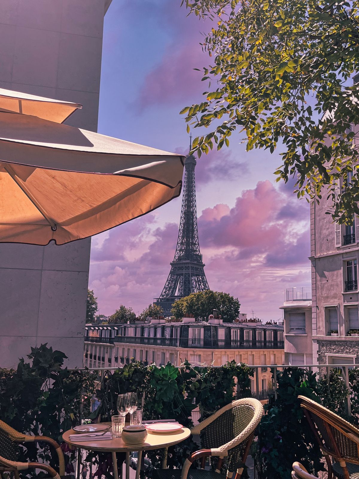 A Parisian café terrace with chairs and tables and the Eiffel Tower in the distance at sunset