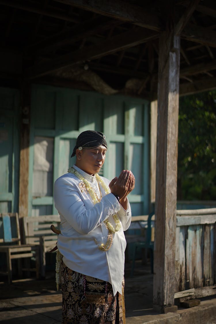 Man In Traditional Clothing Praying Near Wooden House