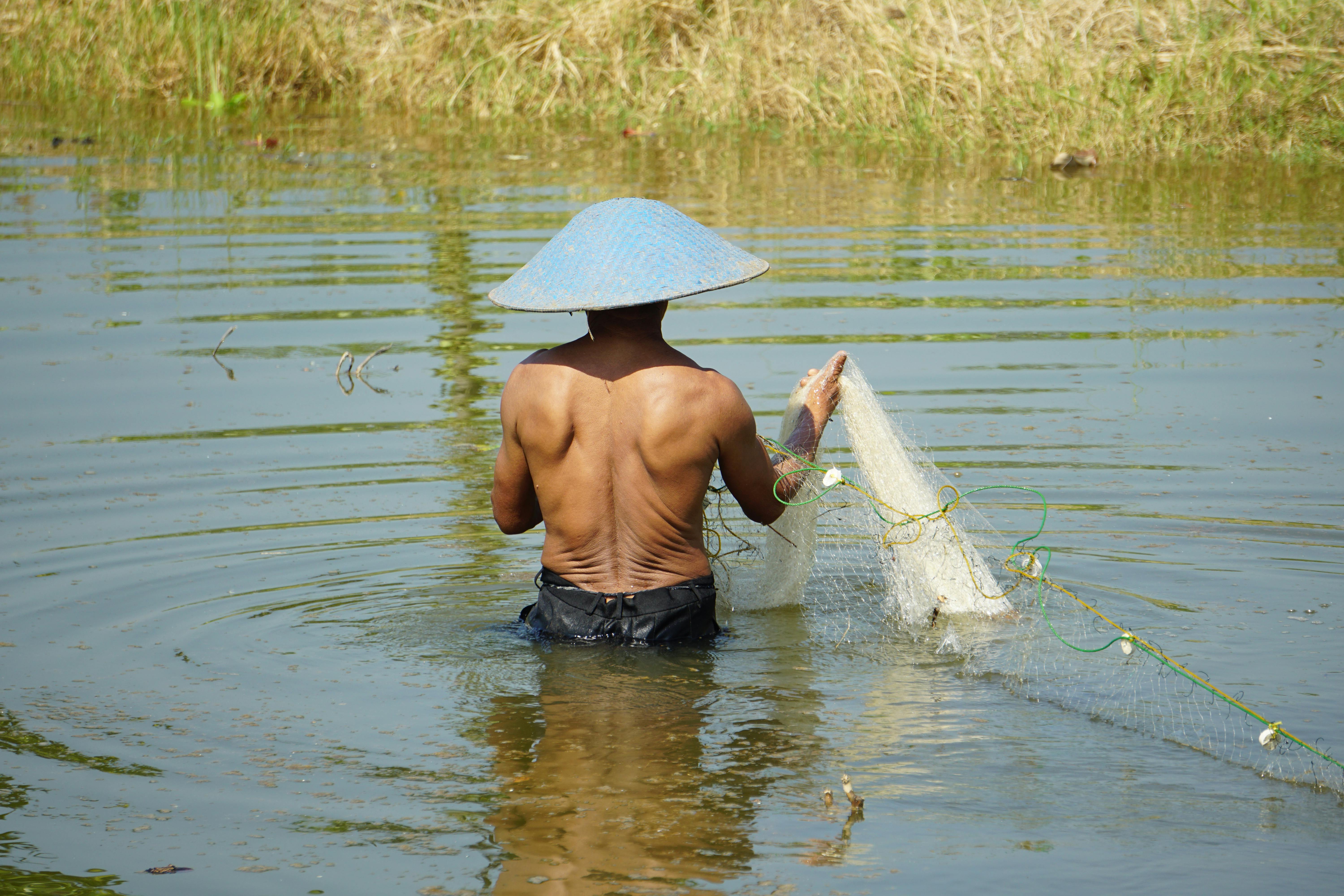Shirtless Man Walking on Water Holding White Fish Net · Free Stock Photo