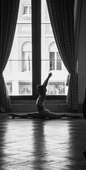 A silhouette of a dancer performing splits in a studio, captured in a dramatic black and white style.