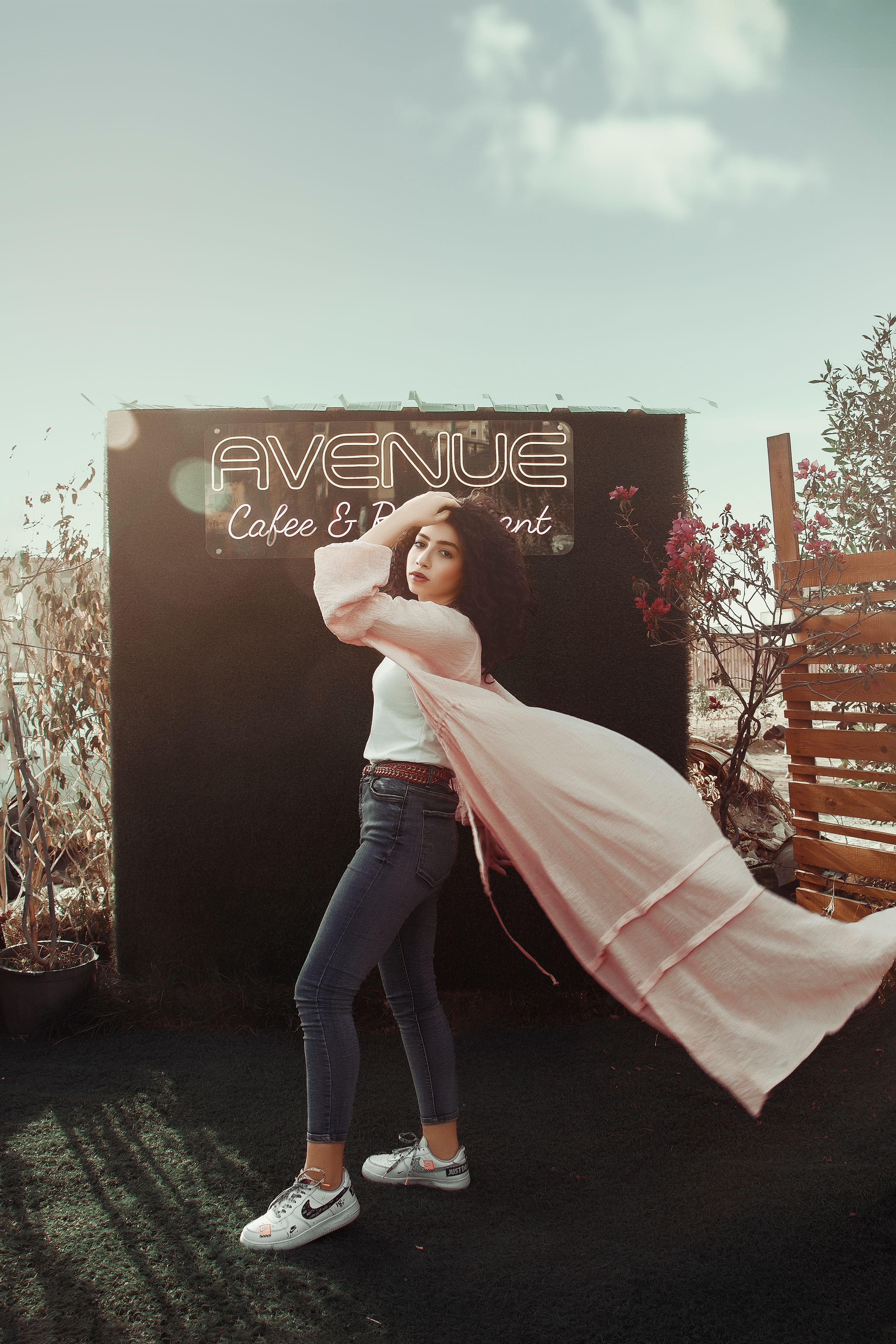 Fashionable young woman strikes a dynamic pose outdoors in front of neon signage.
