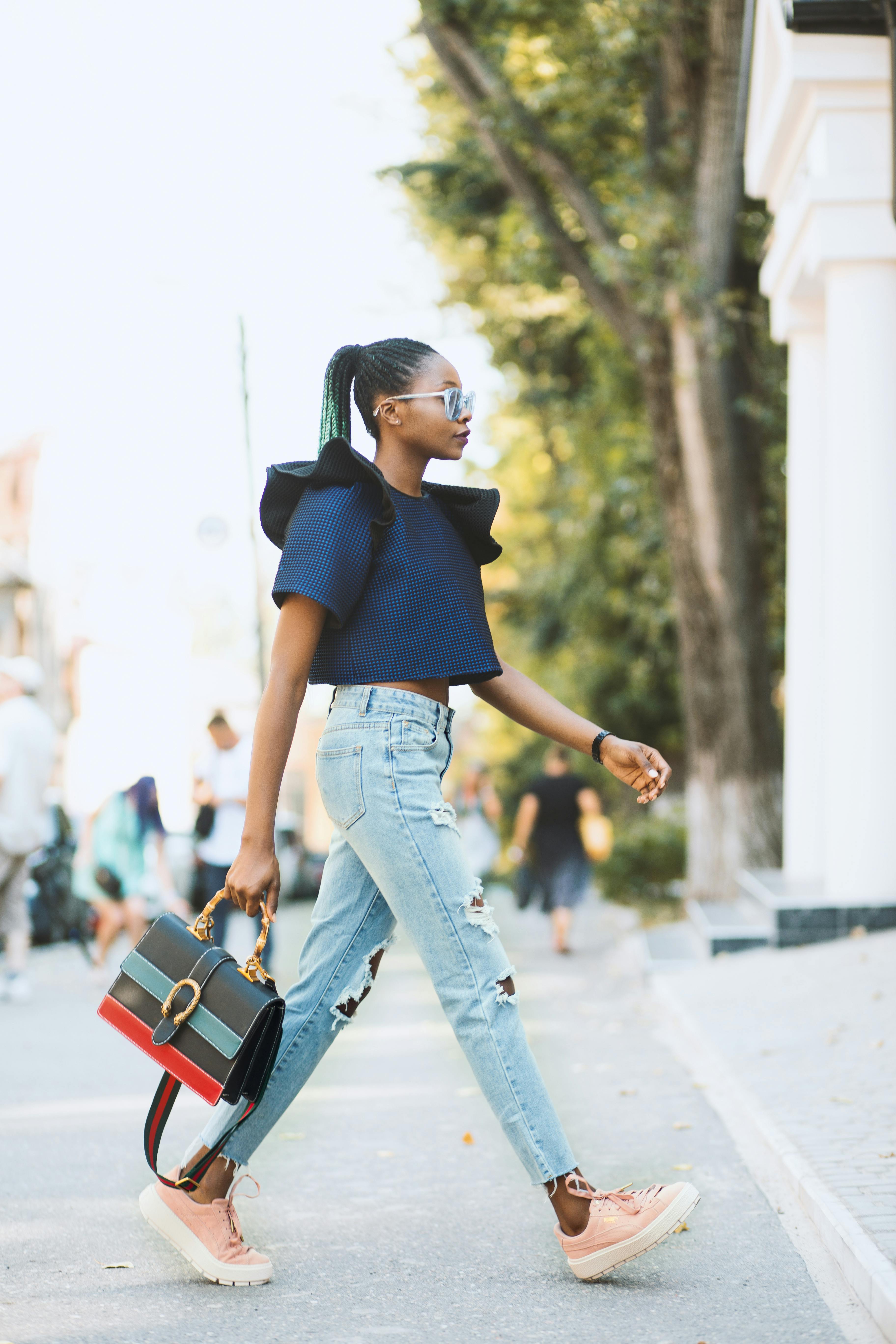 woman in blue crop top and distressed blue denim jeans holding black handbag walking on road