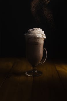 Elegant glass mug of hot chocolate topped with whipped cream on a wooden surface.