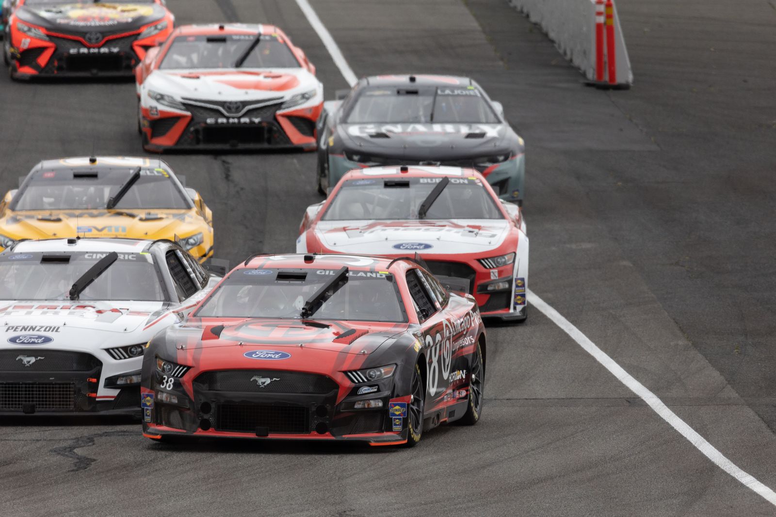 Stock cars racing in a tight pack through a corner