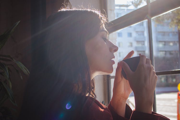 Woman Drinking Hot Beverage By Window