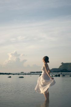 A woman in a white dress stands peacefully by the serene sea in Quang Ngai, Vietnam.