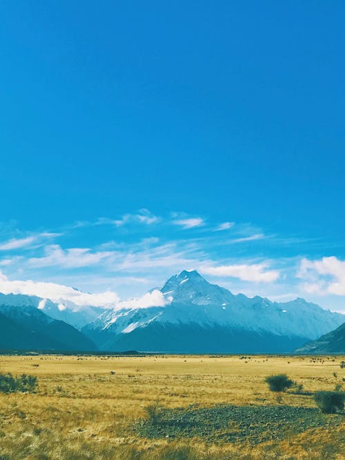 Grass Field Near Mountain Under Clear Blue Sky