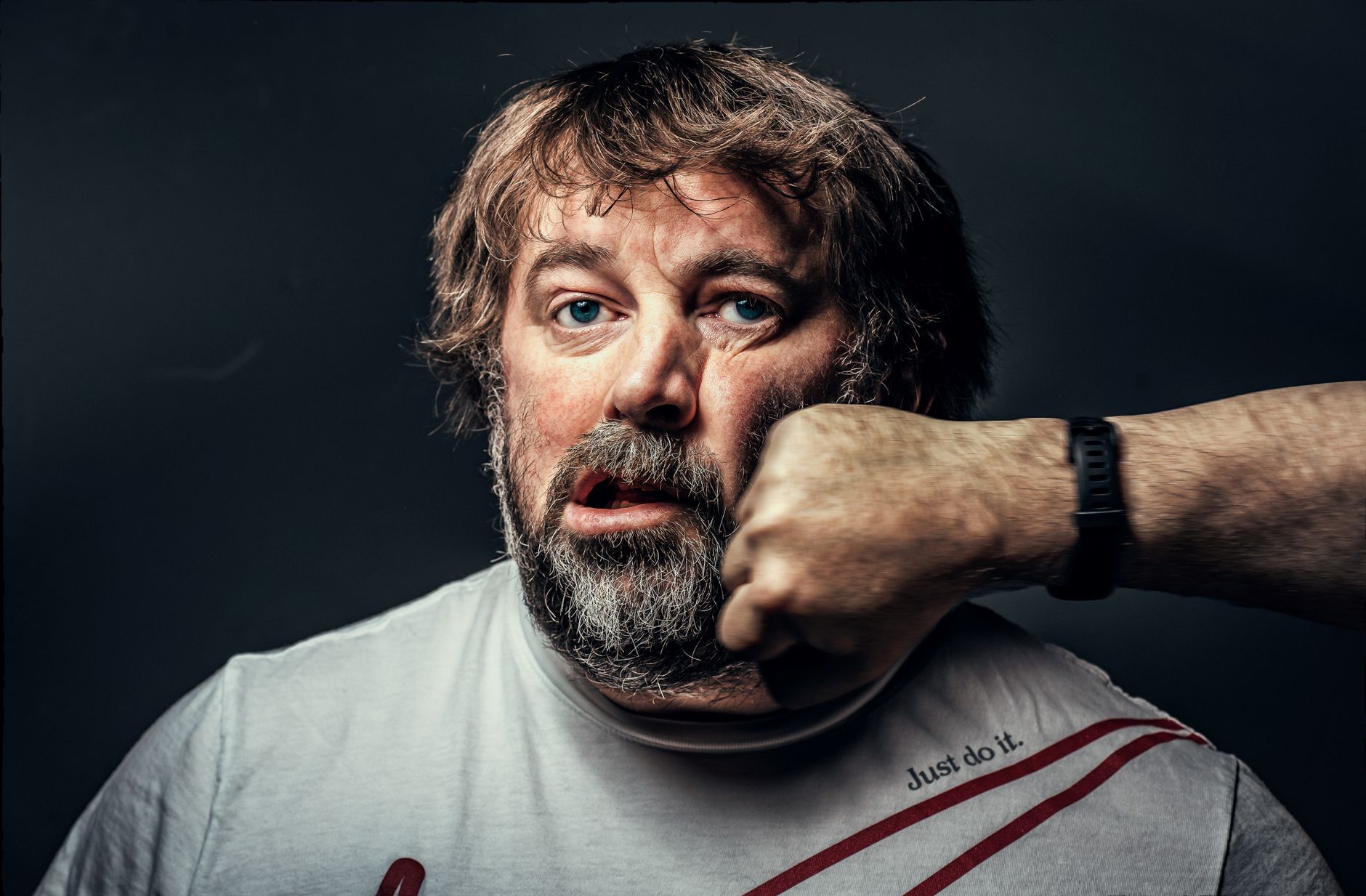 A close-up portrait of a bearded man being punched, showcasing a dramatic expression.