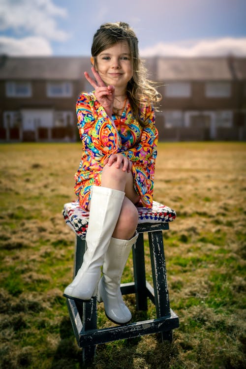 Cute Young Girl sitting on a Wooden Stool and doing a Peace Sign 