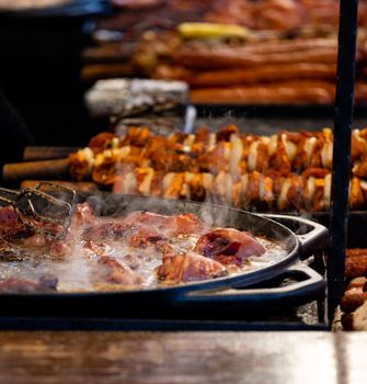 Close-up of frying meat and skewers at a bustling food market, emphasizing rich flavors.