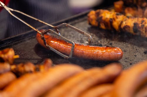 A Tongs Holding a Grilled Sausage