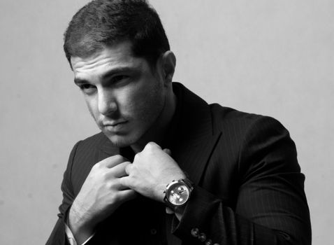 Elegant black and white portrait of a man in a suit adjusting his tie, showcasing a wristwatch.