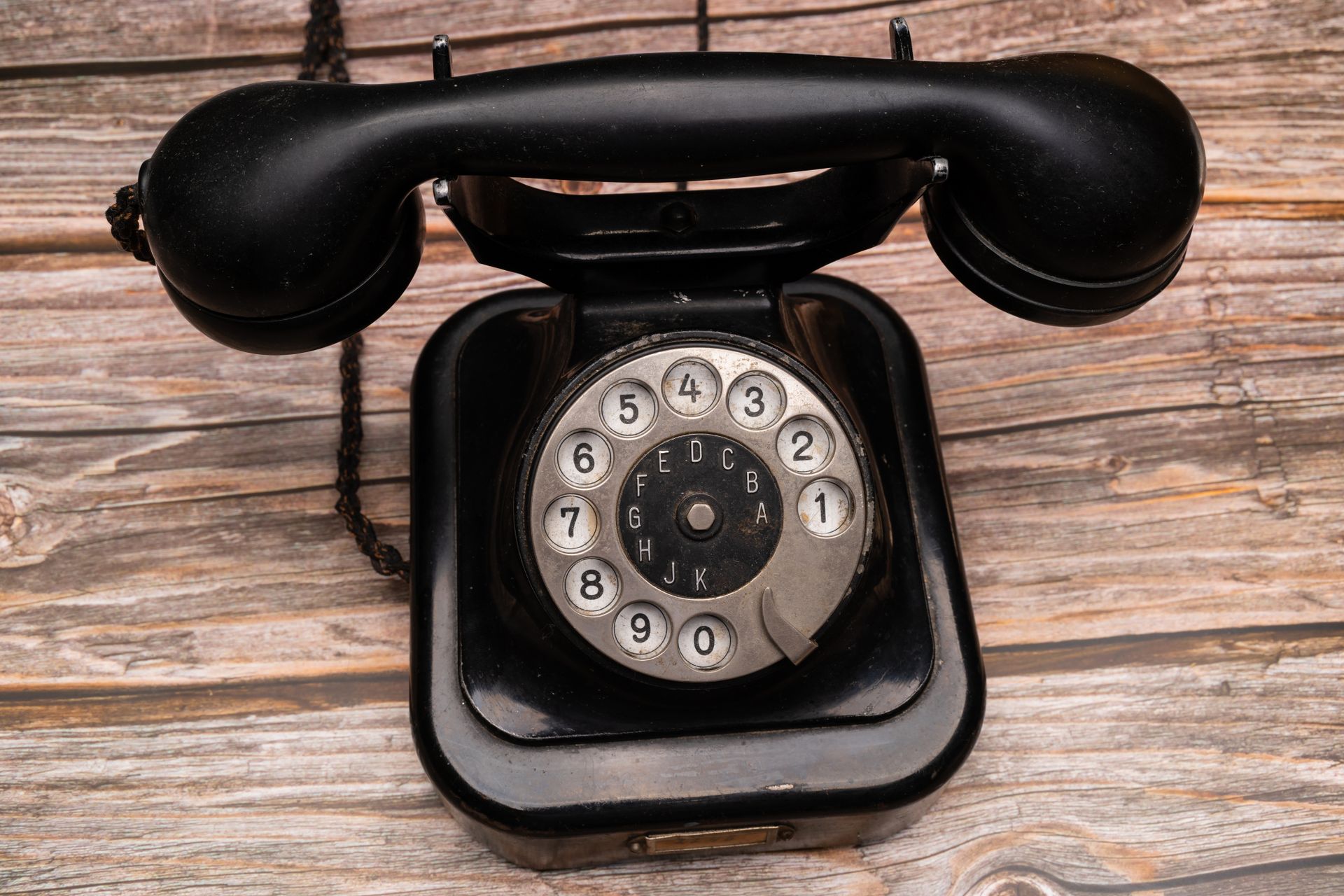 Classic black rotary telephone with dial on wooden background, evoking nostalgia.