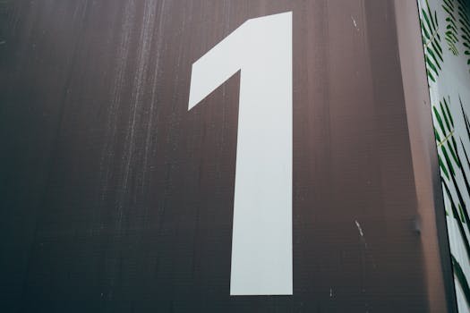 A close-up image of a large, white number one painted on a dark wall.