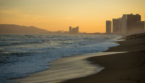 Free A tranquil beach scene with waves and a skyline silhouetted against a warm sunset. Stock Photo