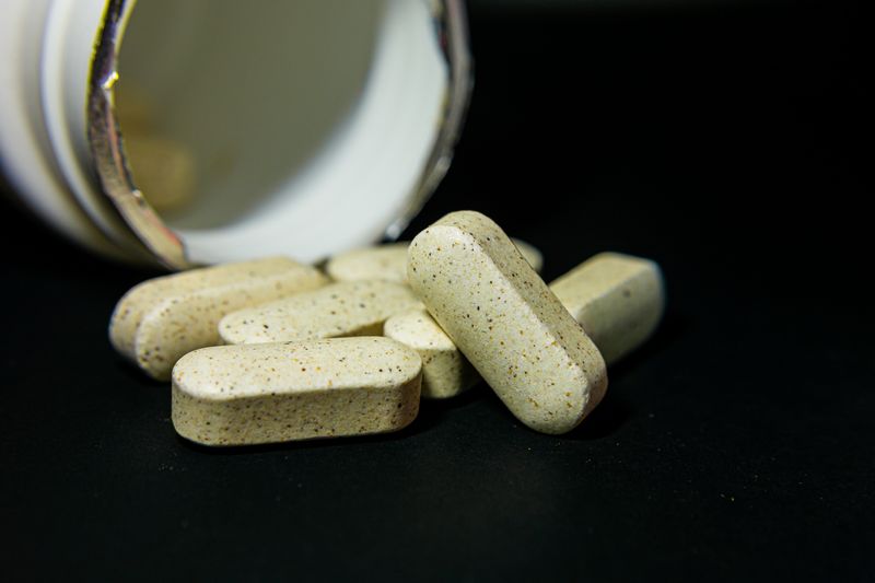 Close-up of white capsule pills spilled from a bottle on a black background. Ideal for health-related visuals.