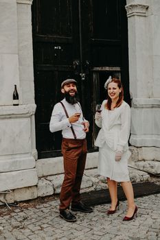 A joyful bride and groom in vintage attire toast with wine outdoors. Celebrating love and style.