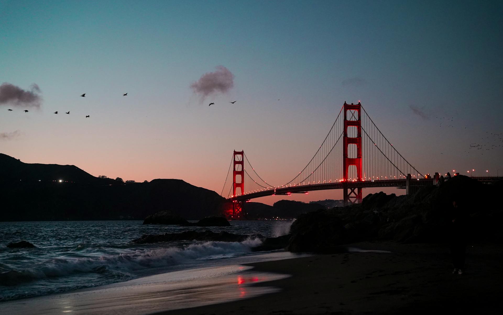 Vue époustouflante du Golden Gate Bridge au crépuscule avec les vagues et les oiseaux qui rehaussent la scène.