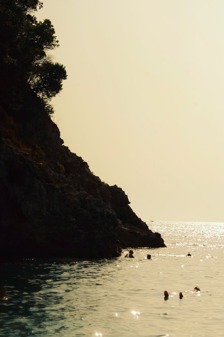 People Swimming In Sea Near Cliff