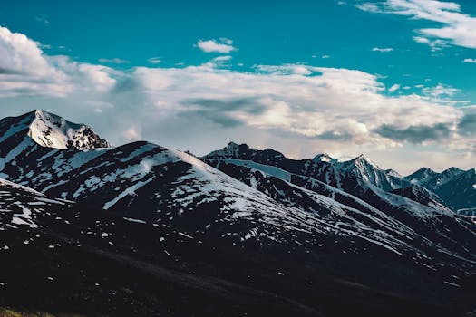 Vast snow-covered mountain range with dramatic clouds in the vast sky.