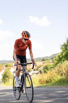 An adult cyclist wearing a helmet rides a road bike outdoors on a rural path.