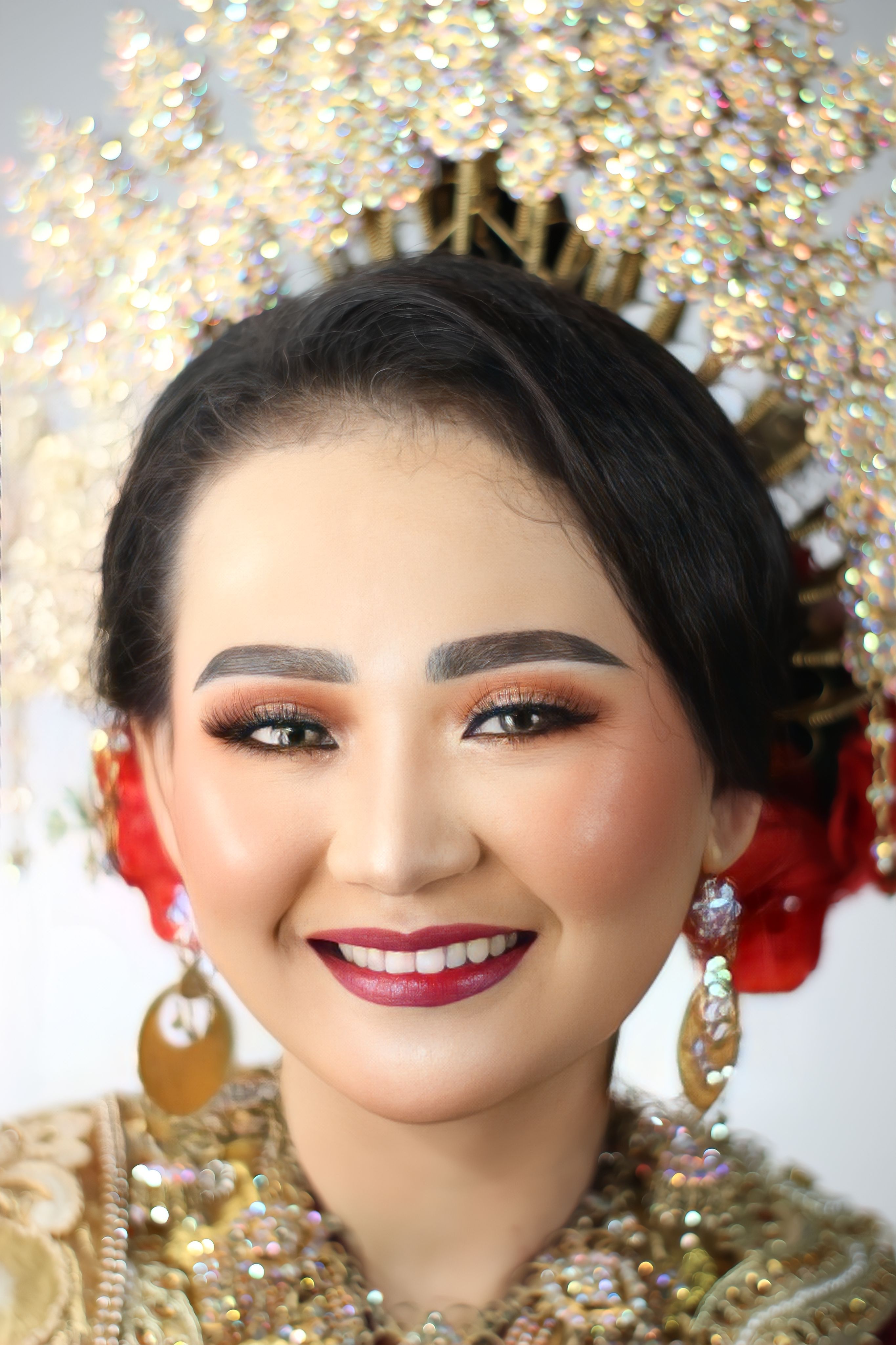 Portrait of a smiling Indonesian bride wearing traditional attire and ornate headpiece.