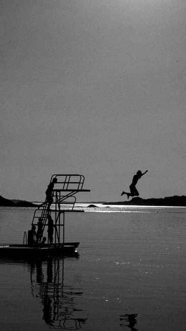 Black and white photo of a boy jumping into water from a platform, capturing summer fun.