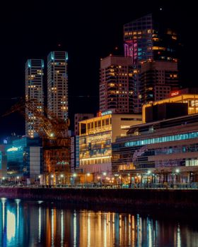 Vibrant cityscape reflecting in water, showcasing modern architecture and night lights.