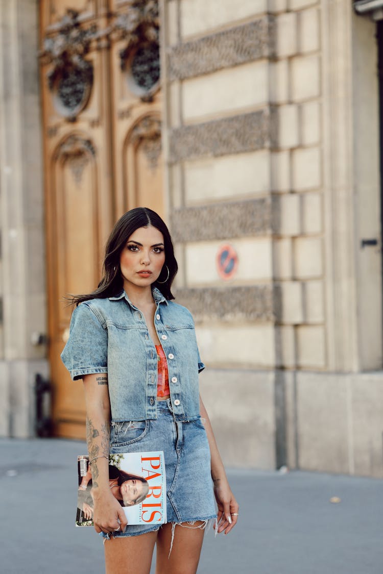 A Woman In A Denim Outfit Holding A Magazine