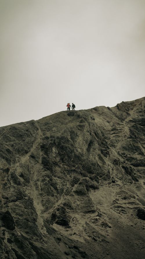 Free Hikers stand atop a rugged mountain in Reykjavík under an overcast sky, capturing the essence of adventure. Stock Photo