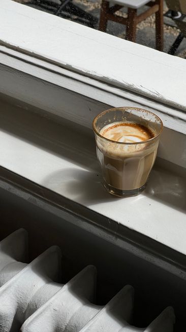 A delicious latte in a glass cup sits on a sunny windowsill, perfect for coffee lovers.