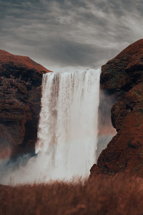 Waterfalls on Brown Rocky Mountain Under Cloudy Sky