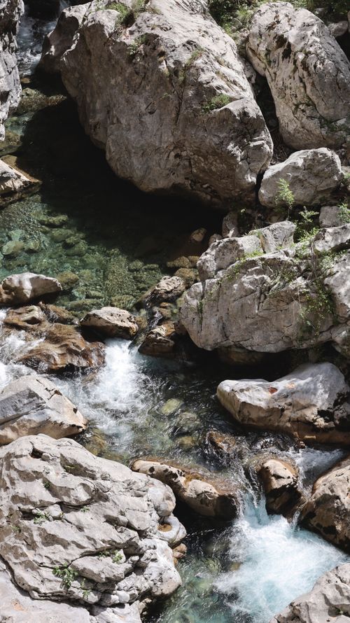 Free A tranquil stream flowing through rugged rocks in a serene mountain landscape. Stock Photo