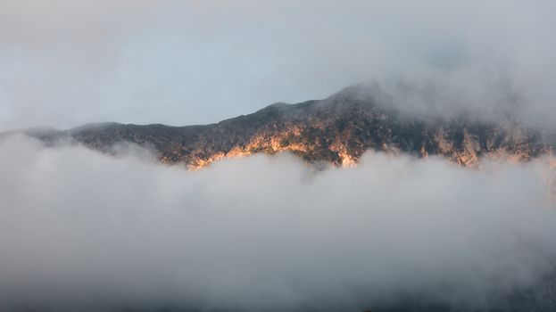 A stunning view of a mountain peak illuminated by dawn light, surrounded by dense fog.
