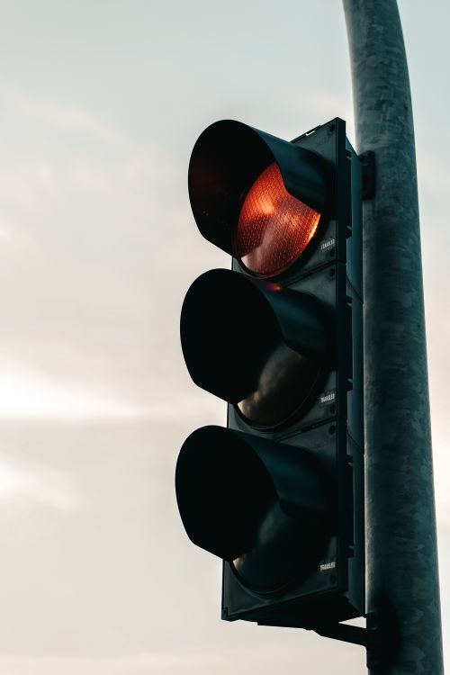 Free A close-up view of a red traffic light against an overcast sky, symbolizing caution and stop. Stock Photo