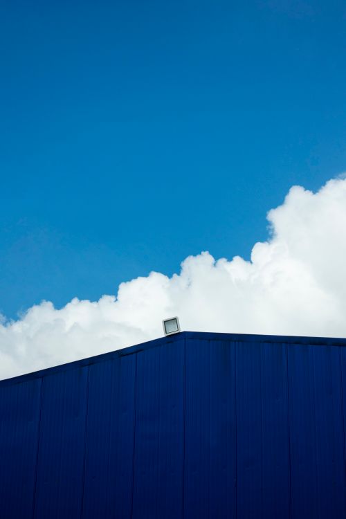 Free Minimalist architectural shot of a blue building facade set against a crisp, cloud-filled sky. Stock Photo